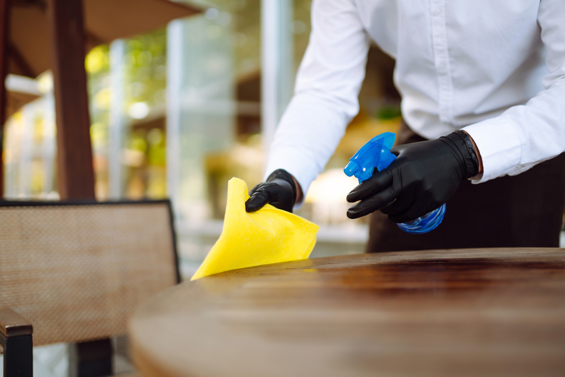 Sanitizing surfaces cleaning  table with disinfectant spray bottle washing surface with towel and gloves. COVID-19 prevention.